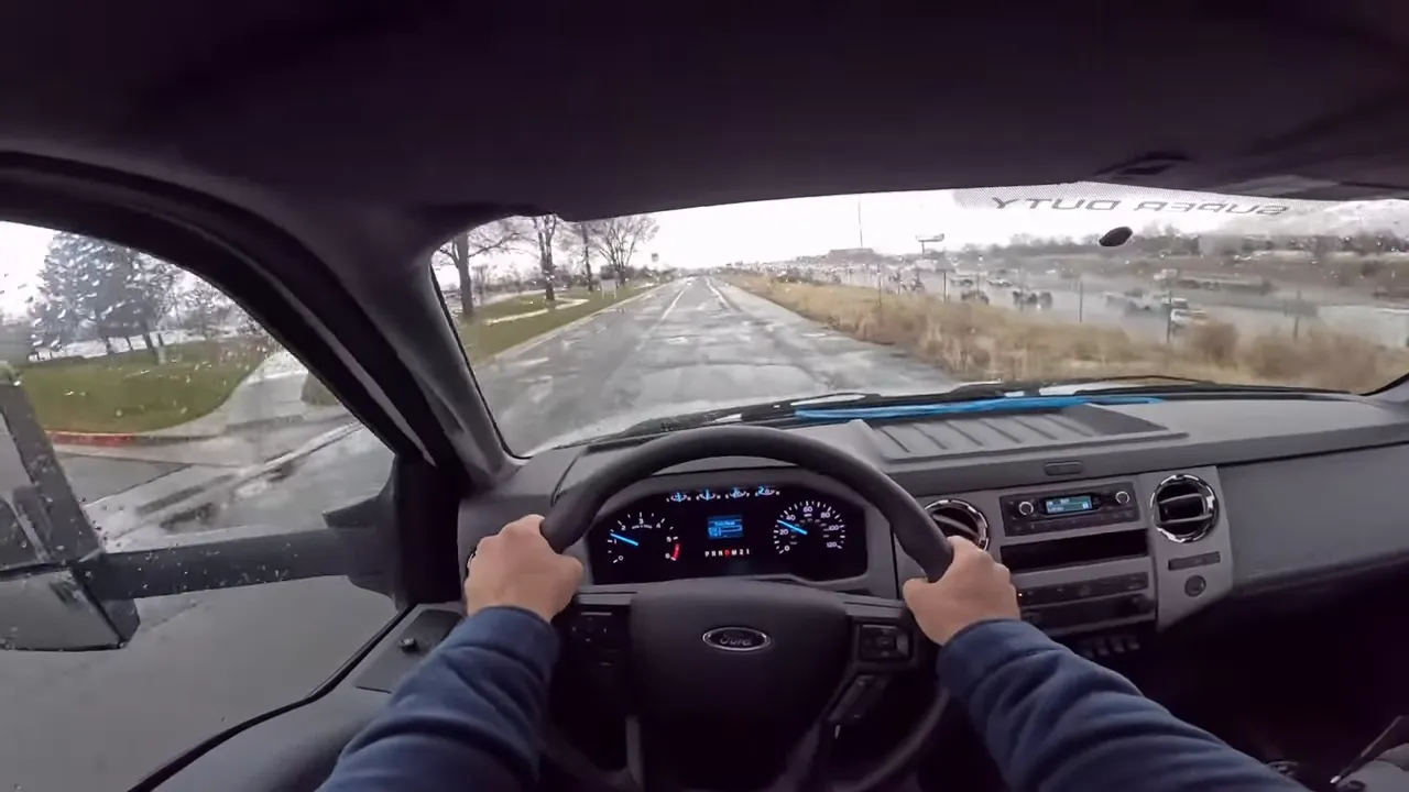 Centered driver view of Ford F-650 steering wheel, dashboard and a cracked wet road ahead illustrating unloaded dynamics.