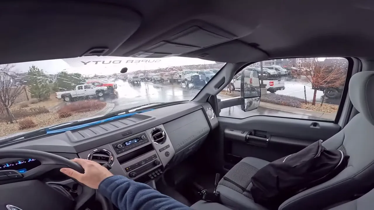 Wide interior view of a Ford F-650 showing the dashboard, steering wheel with hand, passenger seat and side mirror.