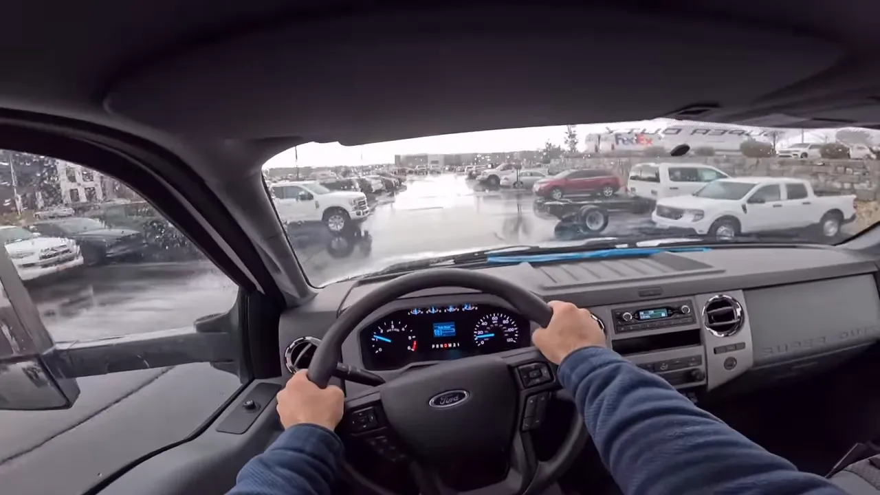 Centered driver point-of-view in a Ford F-650 with clear instrument cluster and view of the wet parking lot ahead.