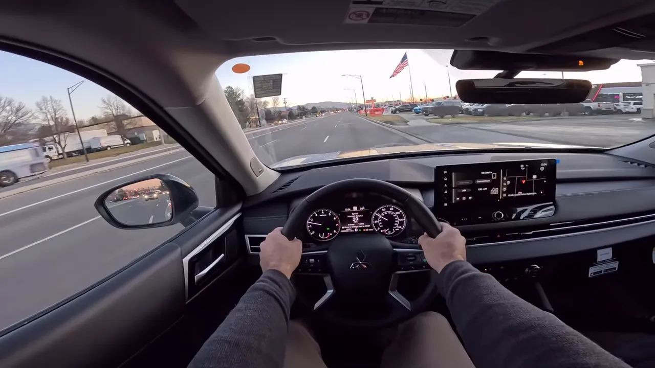Centered driver's view inside 2026 Mitsubishi Outlander showing steering wheel, instrument cluster and infotainment screen with the road ahead