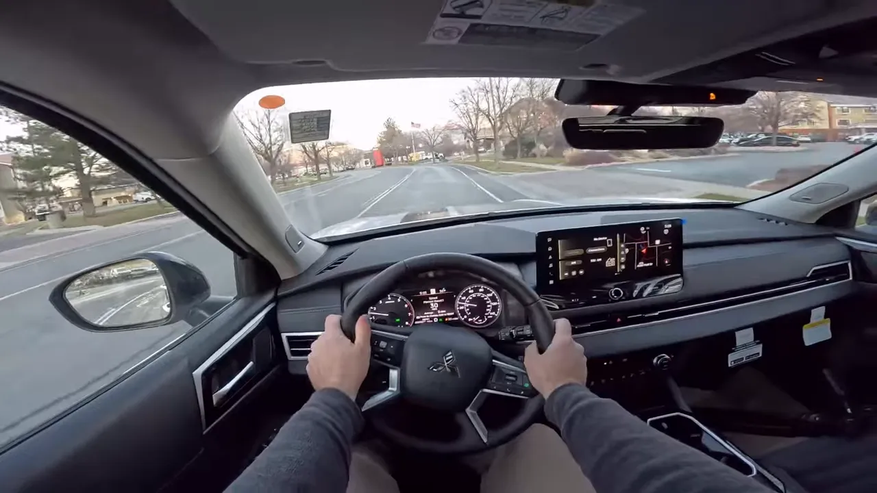 Centered driver's view inside 2026 Mitsubishi Outlander showing hands on wheel, instrument cluster and infotainment screen with the road ahead