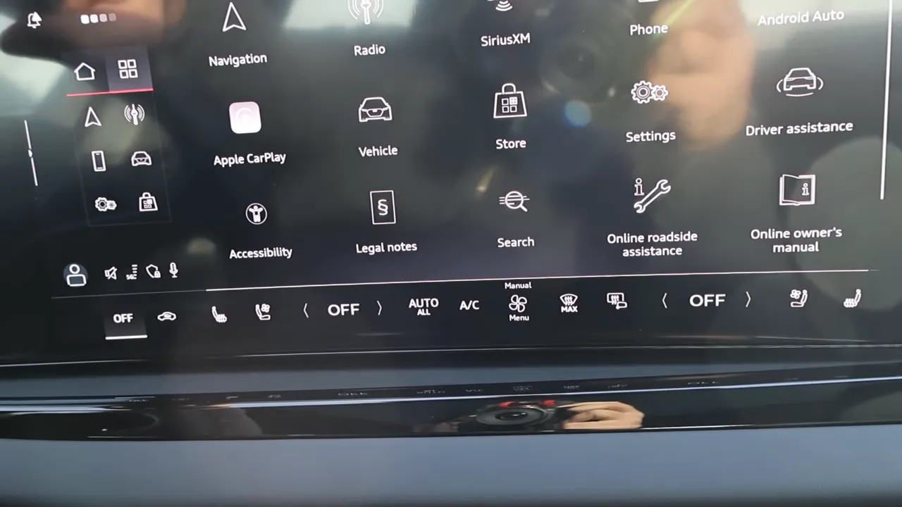 Audi A6 infotainment home screen showing app icons (Apple CarPlay, Navigation, Settings) and the lower touchscreen climate-control bar.