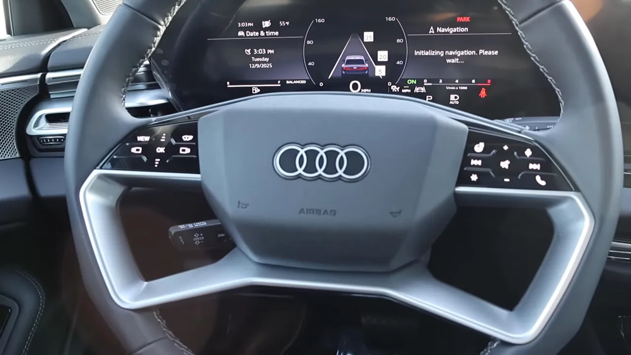 Front view of Audi A6 two‑spoke steering wheel showing audio and climate controls with the digital instrument cluster visible