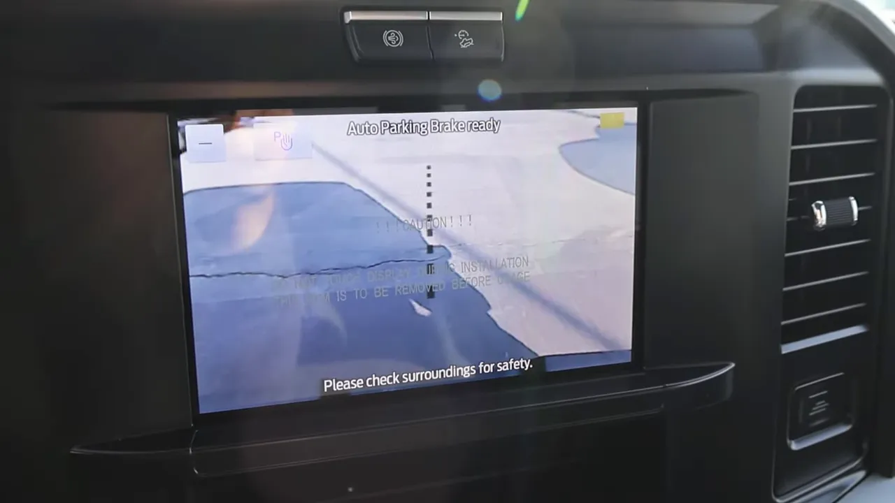 Infotainment screen showing the Ford backup camera view and a 'Please check surroundings for safety' message.