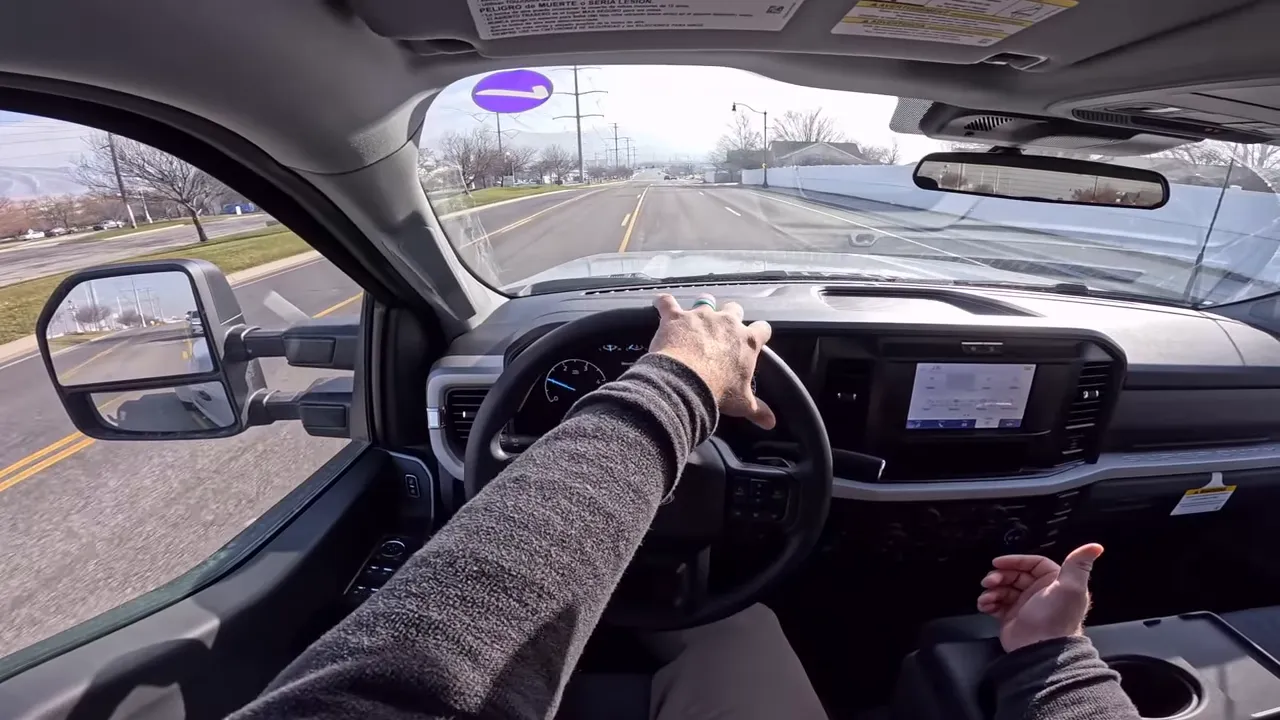 Driver POV of Ford F-350 with left hand on the steering wheel, right hand gesturing and the road ahead visible.