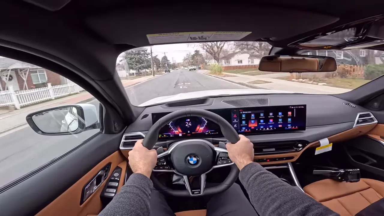 On-road driver view inside 2026 BMW 330i showing steering wheel, digital instrument cluster and road ahead