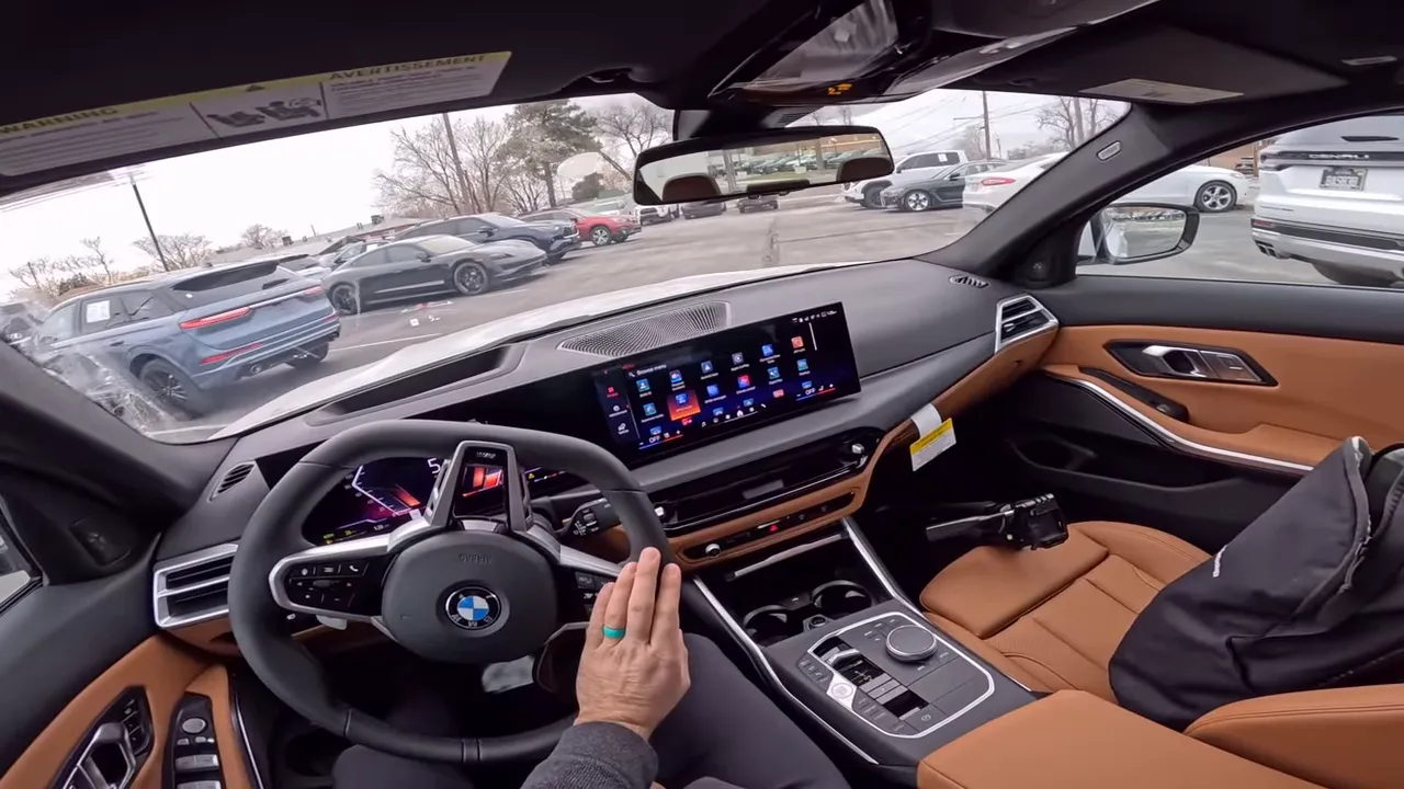 Wide driver-perspective of BMW 330i interior showing steering wheel, center console, iDrive controller and infotainment screen