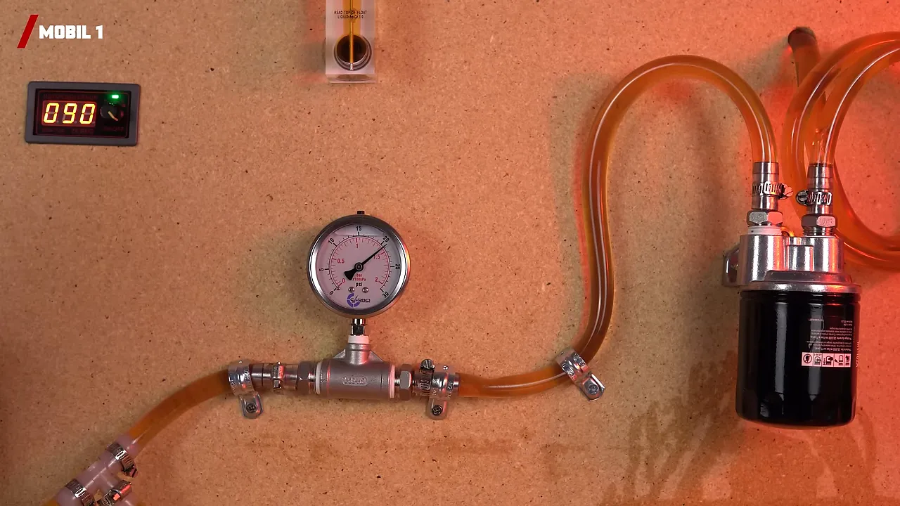 Wide view of the oil flow test rig showing the pressure gauge, orange hoses and mounted oil filter.