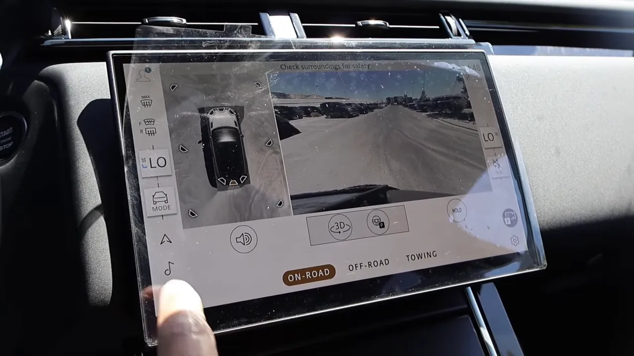 Velar touchscreen with rear camera feed and drive mode buttons; a finger interacting with the display.