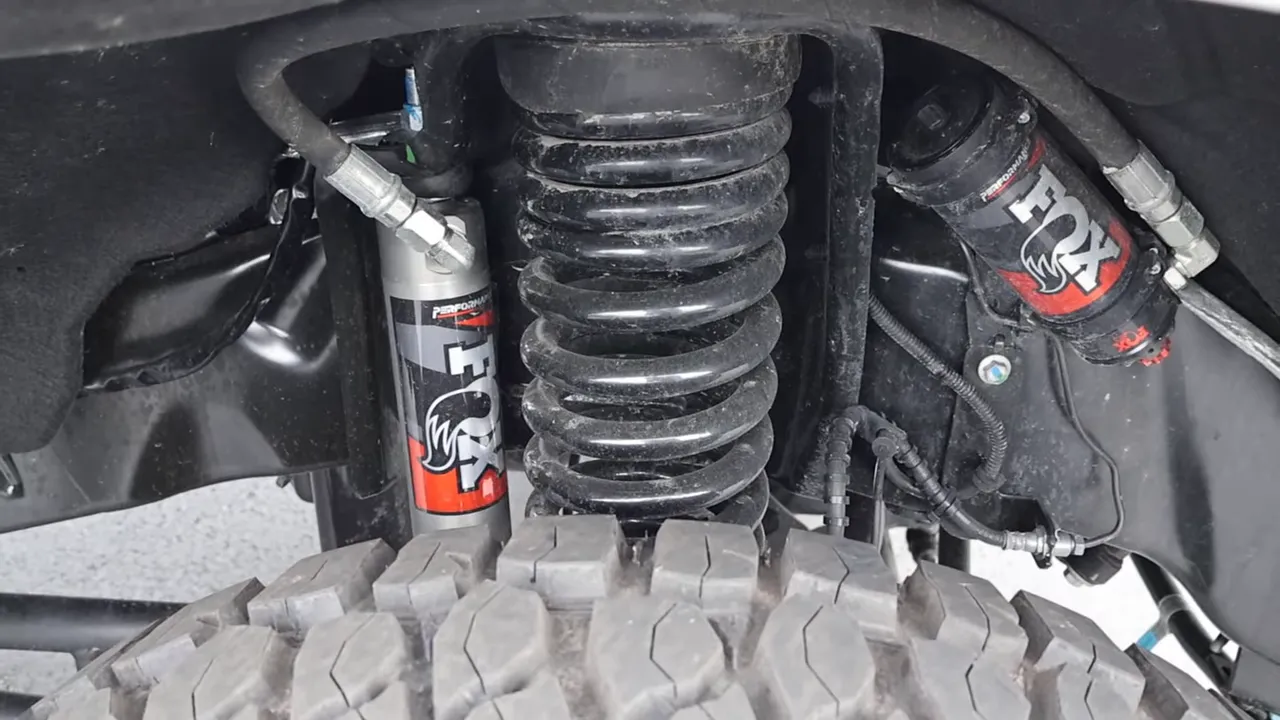 Front suspension close-up showing Fox remote-reservoir shock, coil spring and 35-inch tire