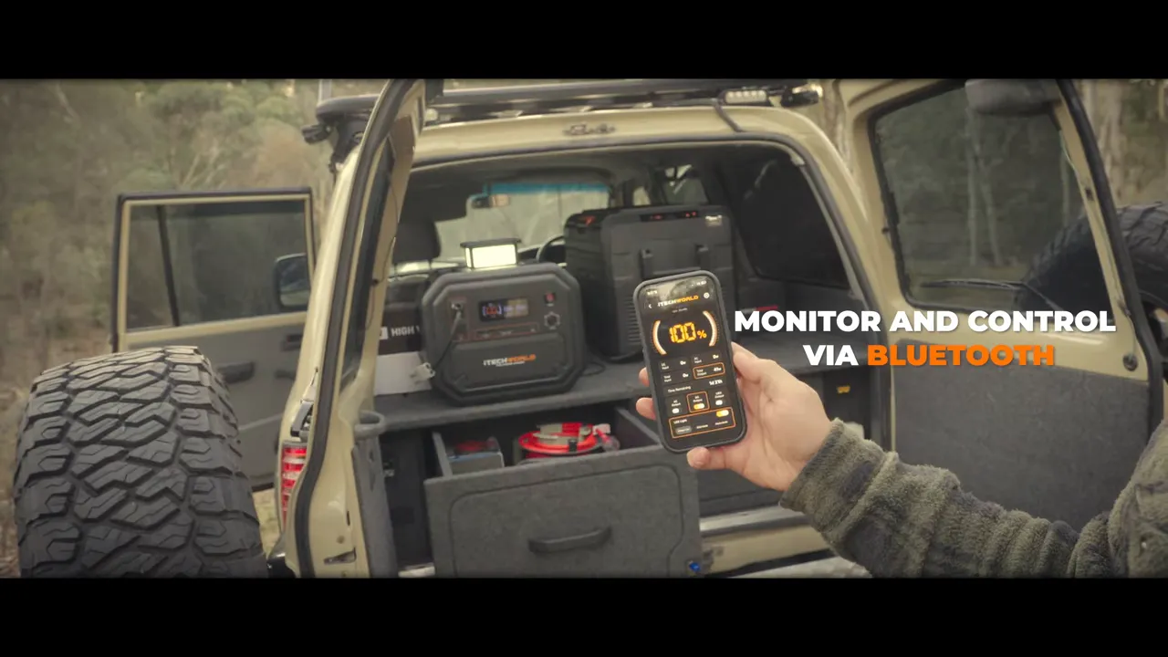 Hand holding a phone with the power station Bluetooth monitoring screen beside an open vehicle rear compartment