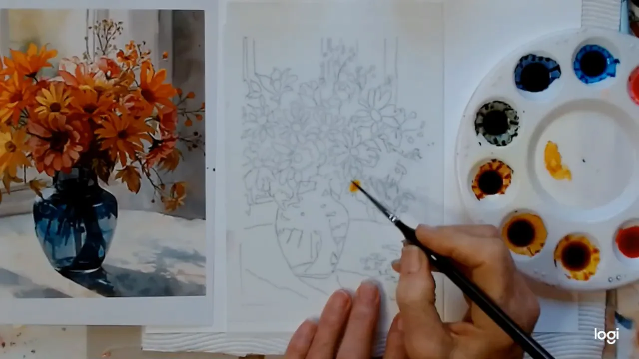 Close overhead view of a brush picking up golden-yellow ink from a palette next to a sketched floral composition and printed reference.