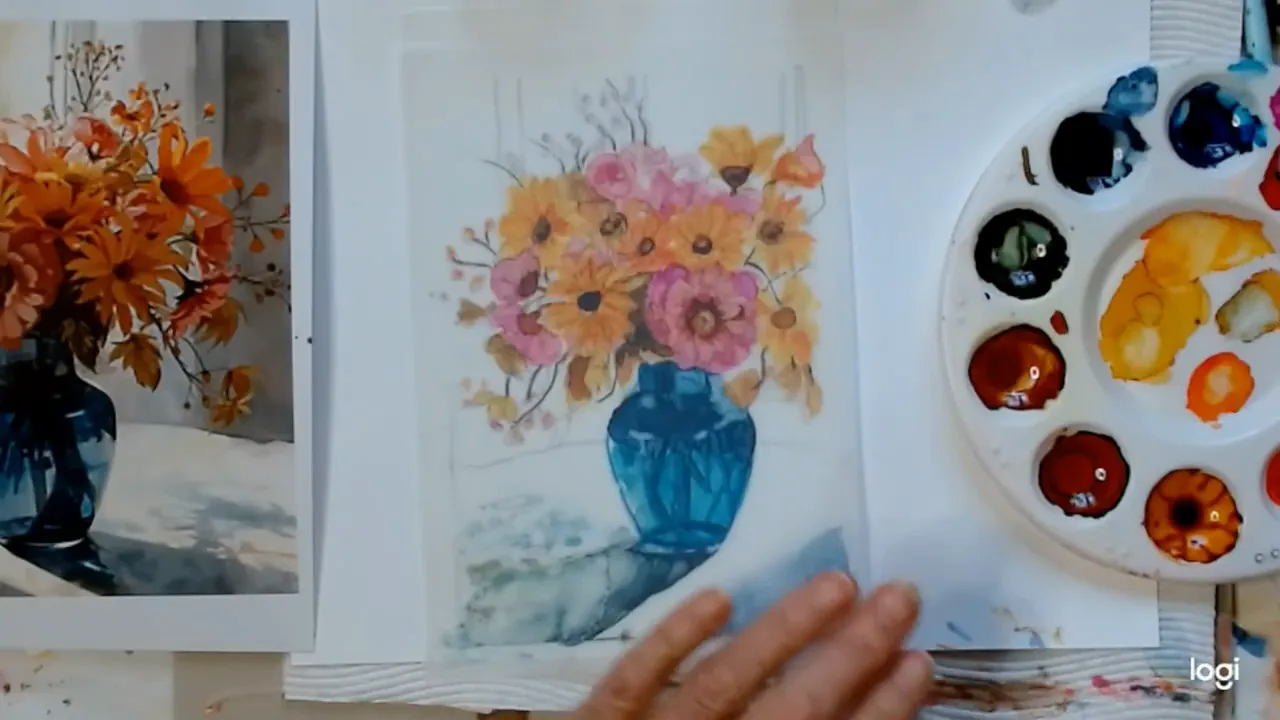 Overhead view of a translucent floral painting with a blue vase centered, paint palette to the right and a hand at the bottom preparing to work or flip the paper.