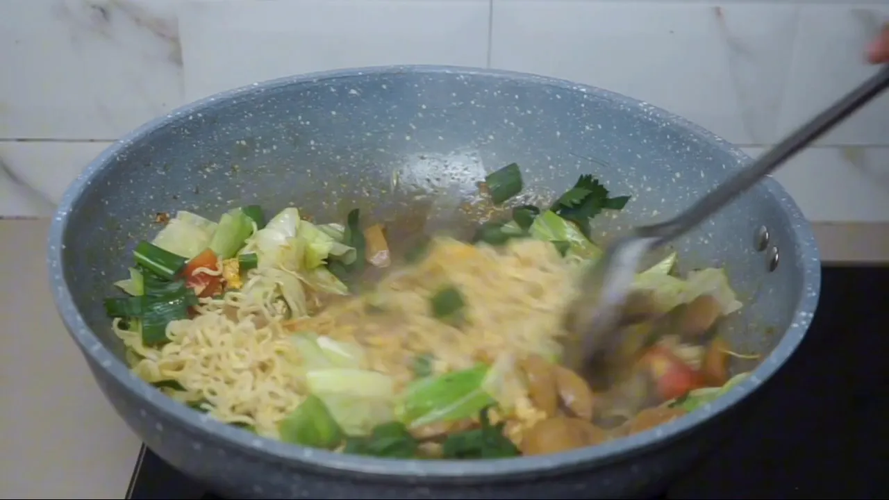 Proses memasukkan sayuran dan mie ke dalam tumisan
