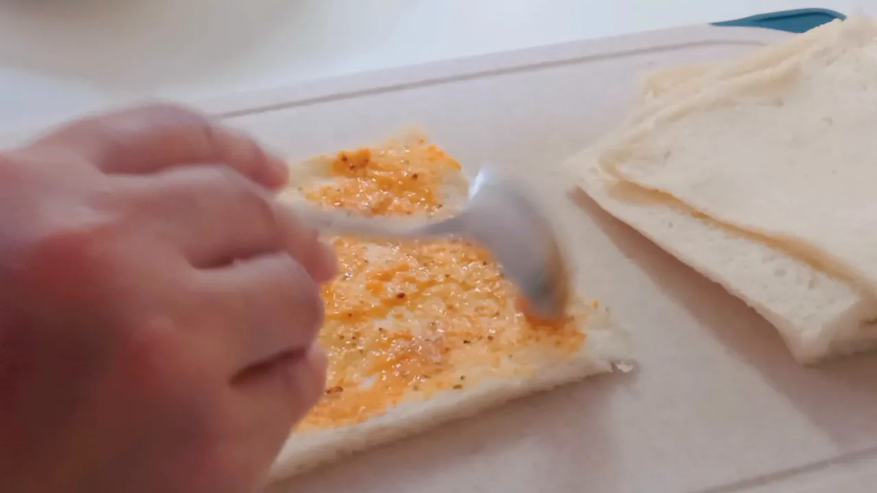 Mengoleskan saus dan menggulung roti bersama sosis dengan perekat putih telur