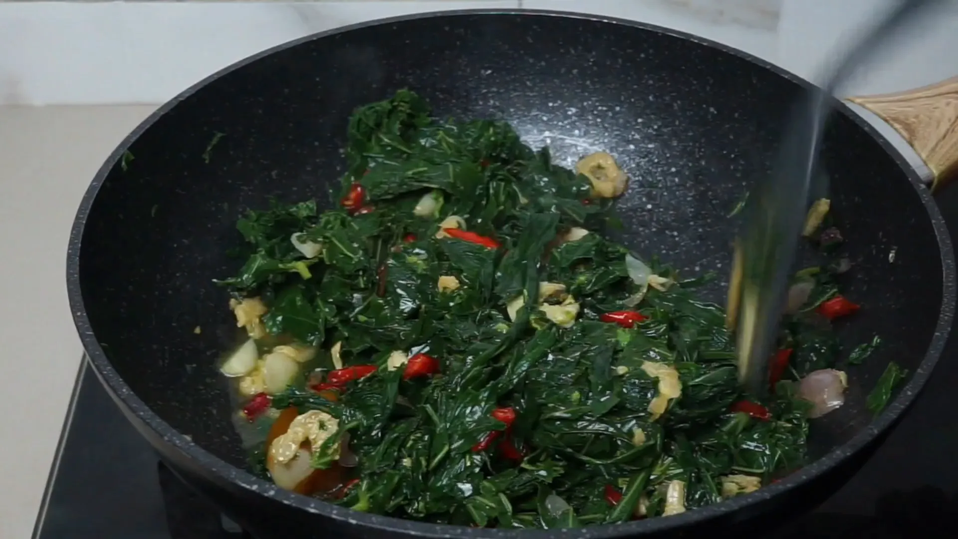 Oseng daun singkong dengan bumbu dan ebi sedang dimasak di wajan