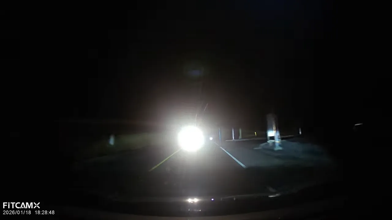 Night dash cam footage with bright oncoming headlights causing heavy glare in the center of the frame