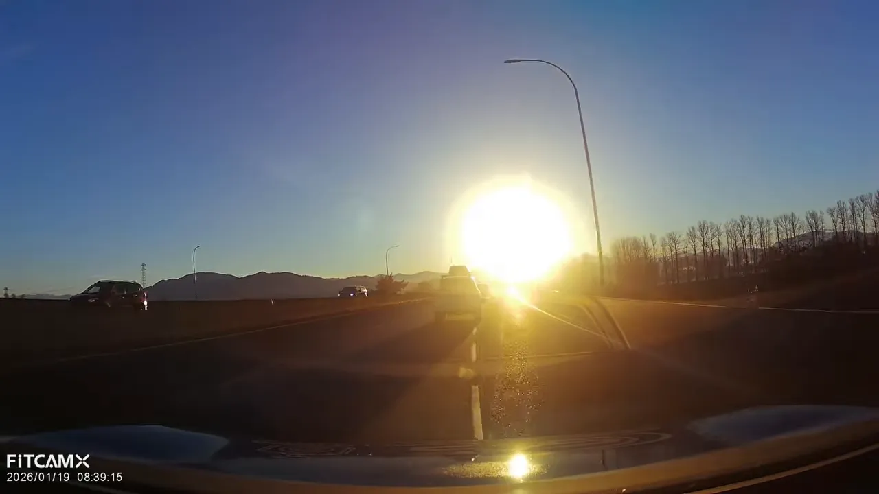Dash cam footage driving directly into a bright low sun with heavy glare obscuring the road ahead