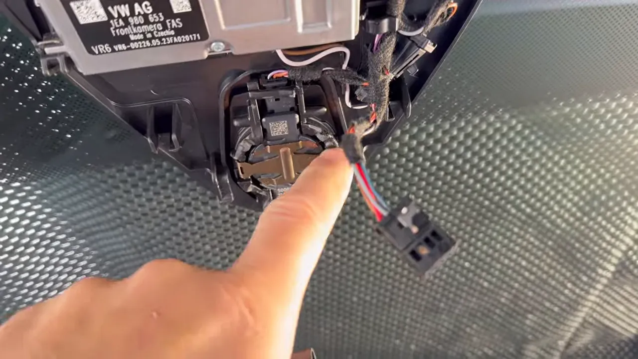 Close-up of mirror housing area with finger pointing to the factory connector behind the rearview mirror