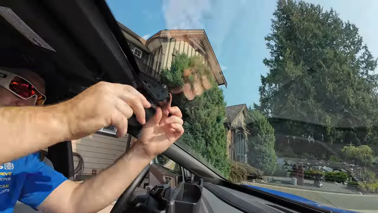 Hands pressing a dash cam mount against the upper windshield