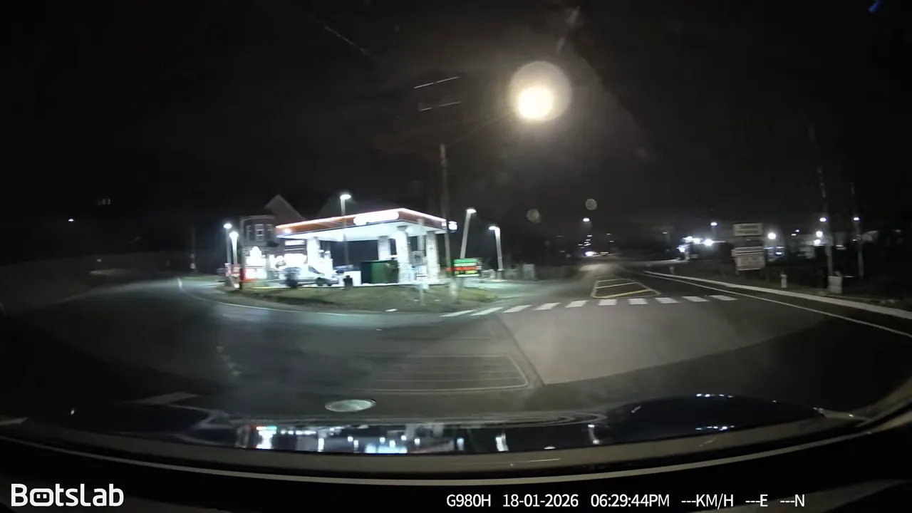 Night driving footage approaching a brightly lit gas station on the left side of the road