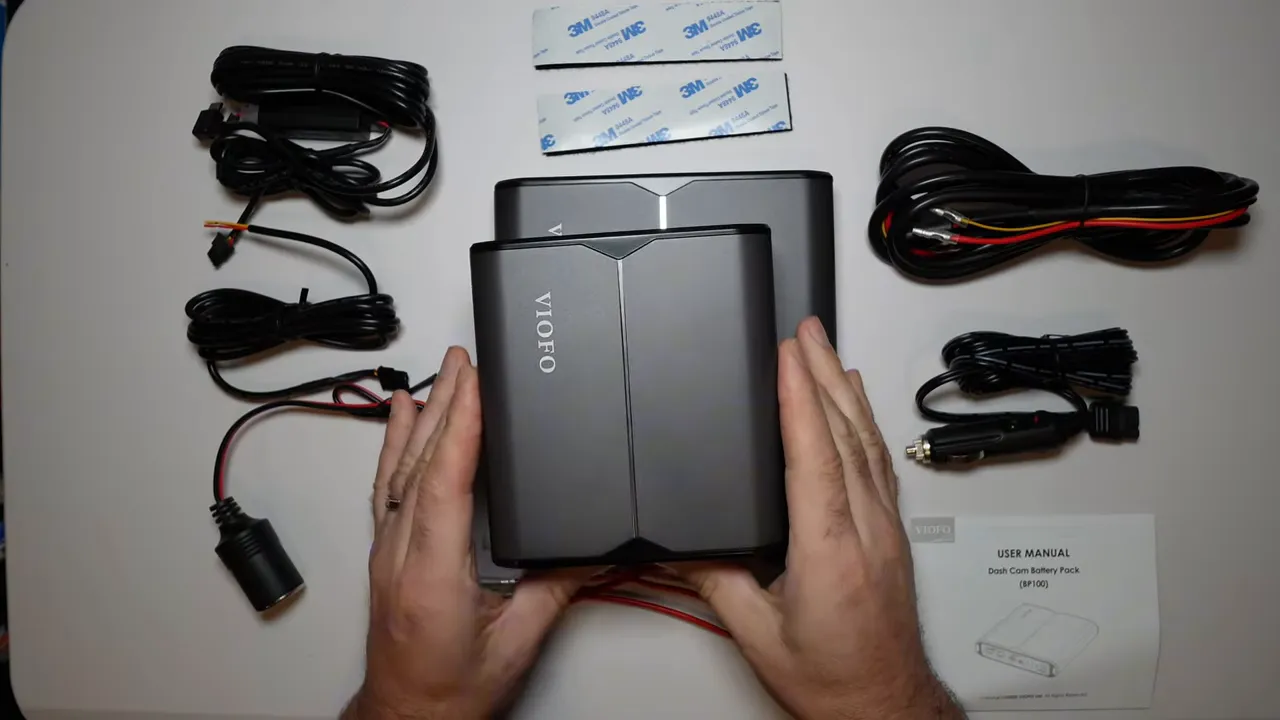 Smaller VIOFO BP60 battery pack held in front of the larger BP100 on a table