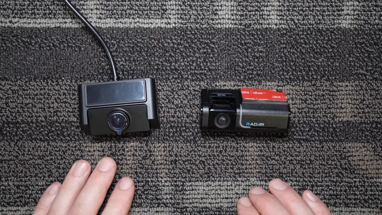 Thinkware rear camera with detachable connector on the left and Vueroid rear camera with integrated cable on the right, placed side-by-side on a carpeted surface