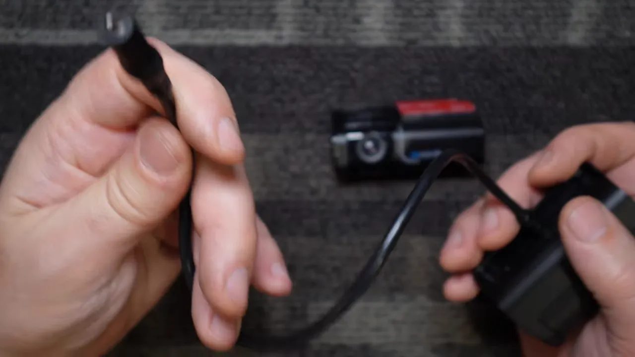 Hand holding the end of a rear camera cable connector with the camera body blurred in the background.