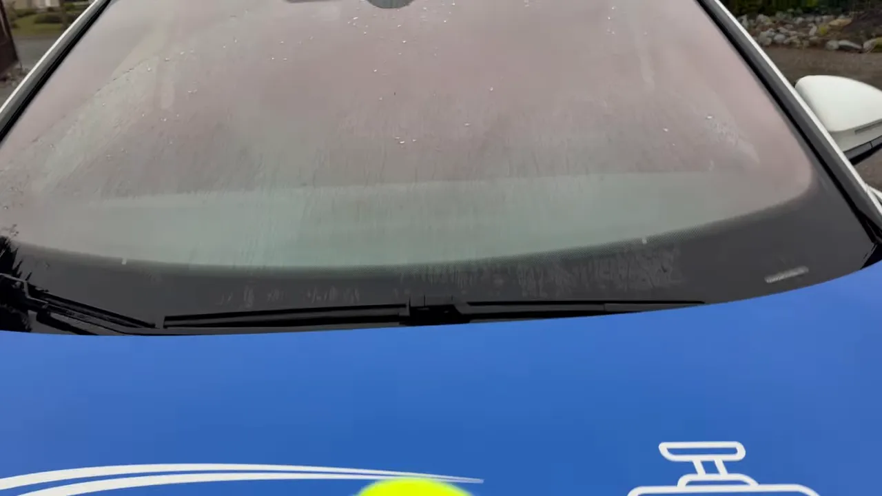 Windshield with rain streaks and blue test-vehicle hood visible