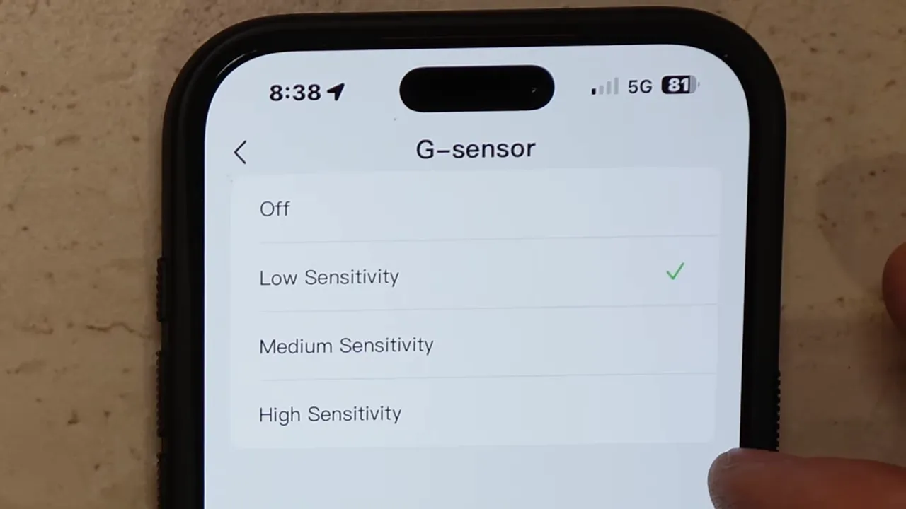 High-quality close-up of the VIOFO app G-sensor menu with Low Sensitivity checked and a small portion of the finger visible