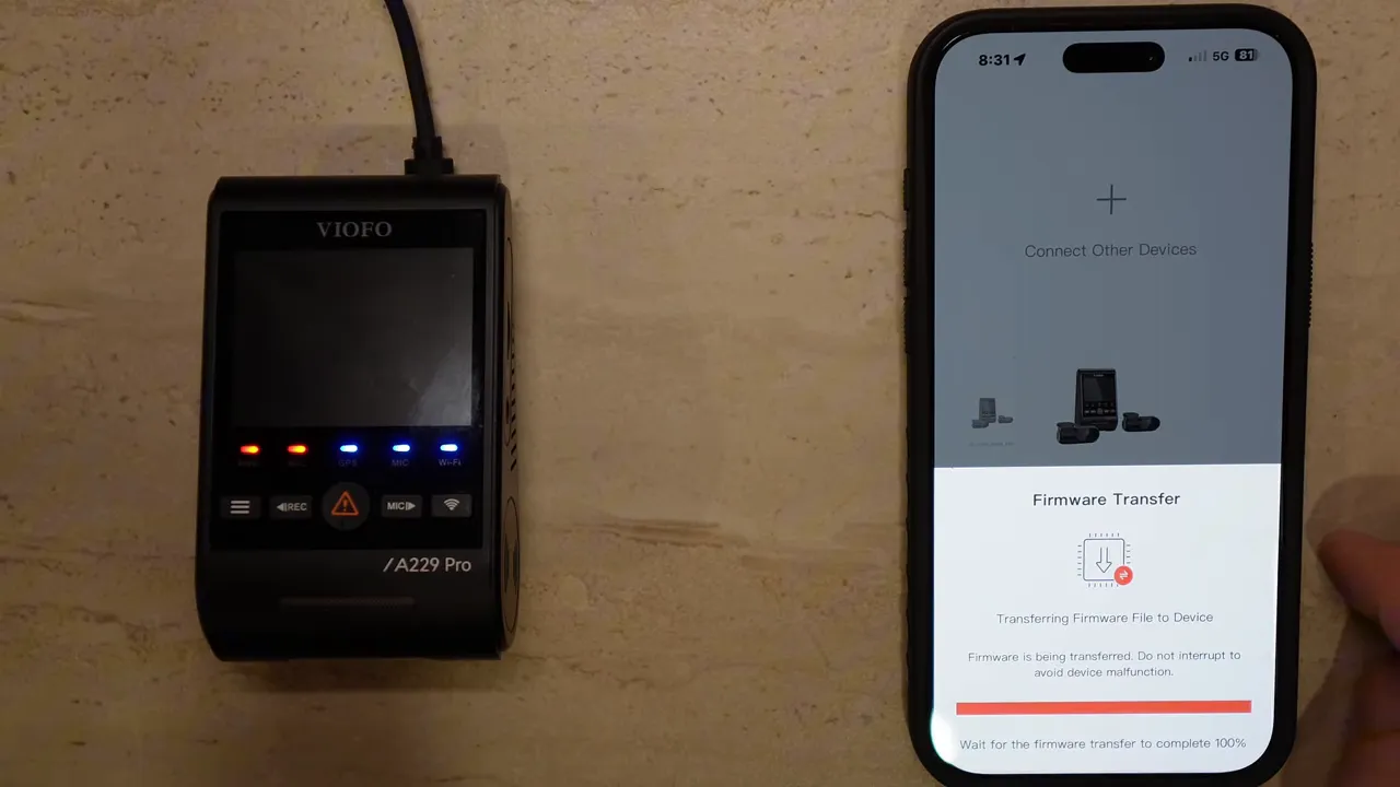 Phone displaying VIOFO app with firmware transfer at 100% next to the powered A229 Pro dashcam