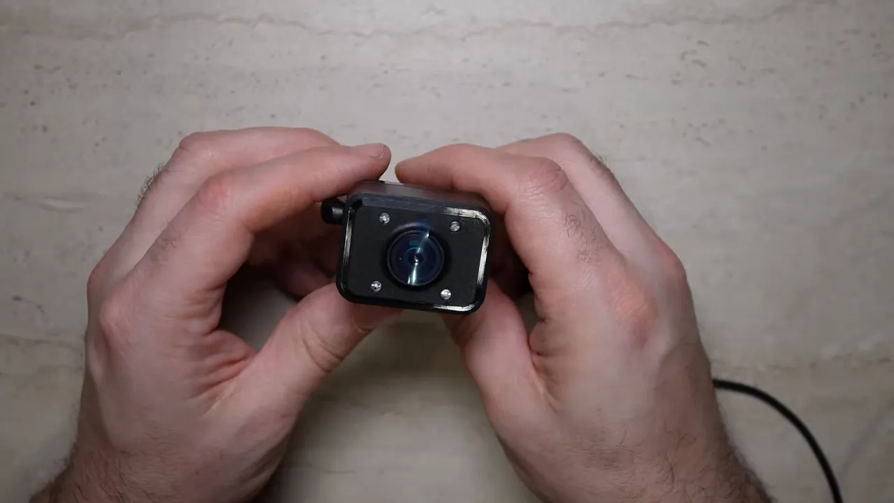 Centered close-up of the Vueroid S1 small interior camera lens and housing held between two hands