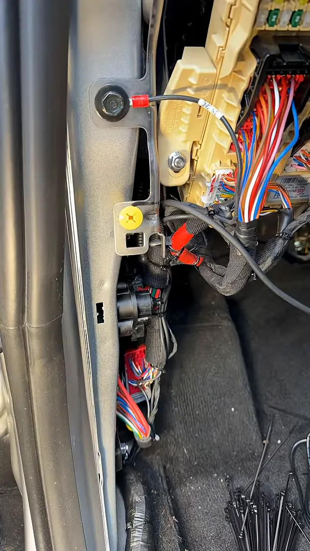 Clear view under the front driver seat of a Hyundai Tucson showing the fuse box, routed wiring harness and zip ties on the floor