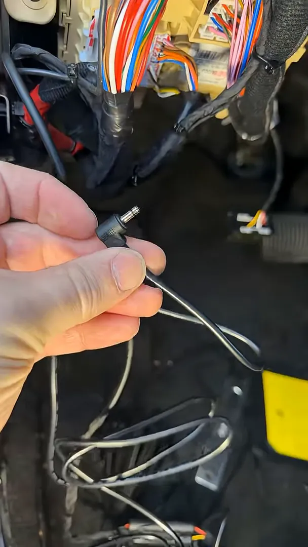Hand holding dash camera DC barrel connector with wiring routed along Hyundai Tucson factory harness ready for final connection