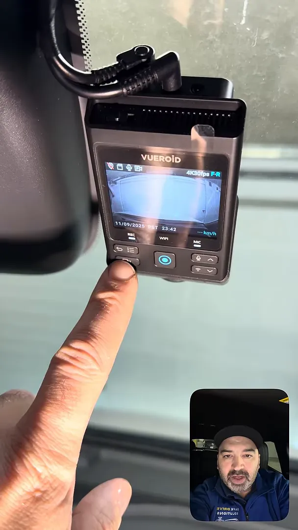 Hand interacting with a Vueroid dash camera buttons while the unit is mounted near the headliner; display shows live view and labels for REC, WIFI and MIC