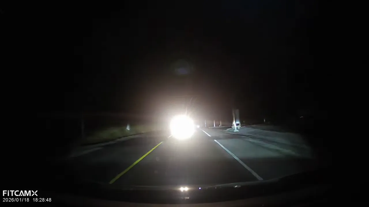 Dash cam night scene with severe headlight glare obscuring roadside details
