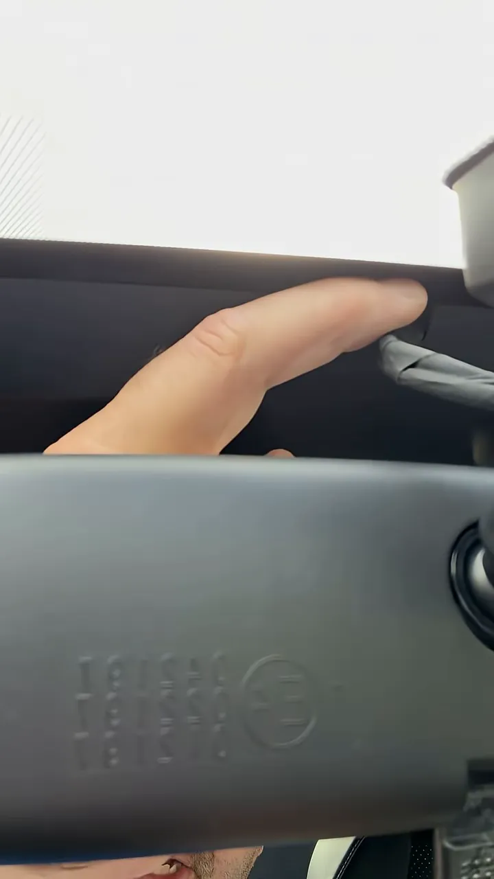 Hand pointing to dash cam cable tucked above the rear-view mirror