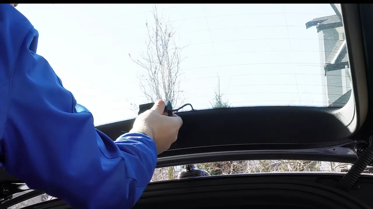 Hands adjusting rear dashcam angle and cable at the Audi A5 hatch with mount visible