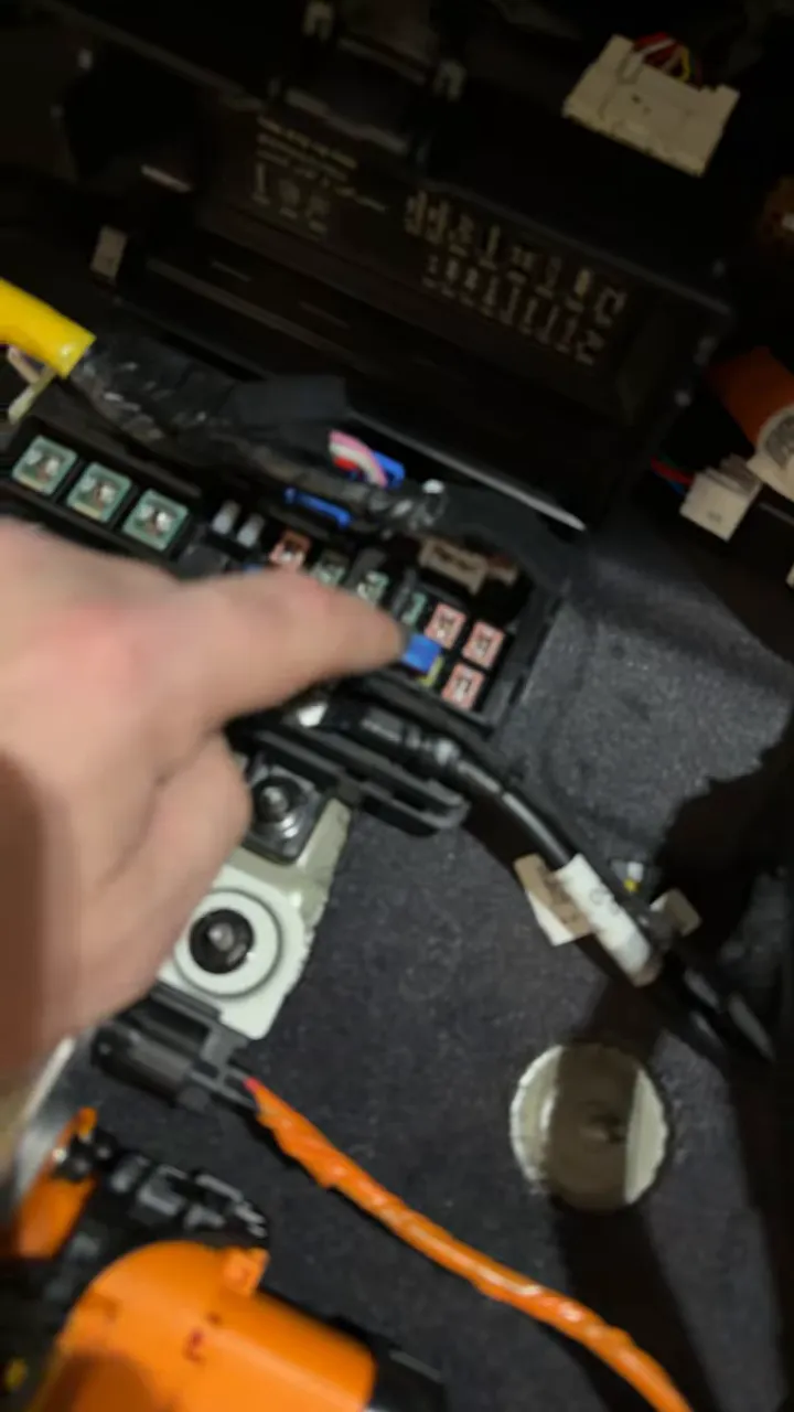 Finger pointing at spare fuse slots in the Kia EV9 rear fuse block behind the trim.