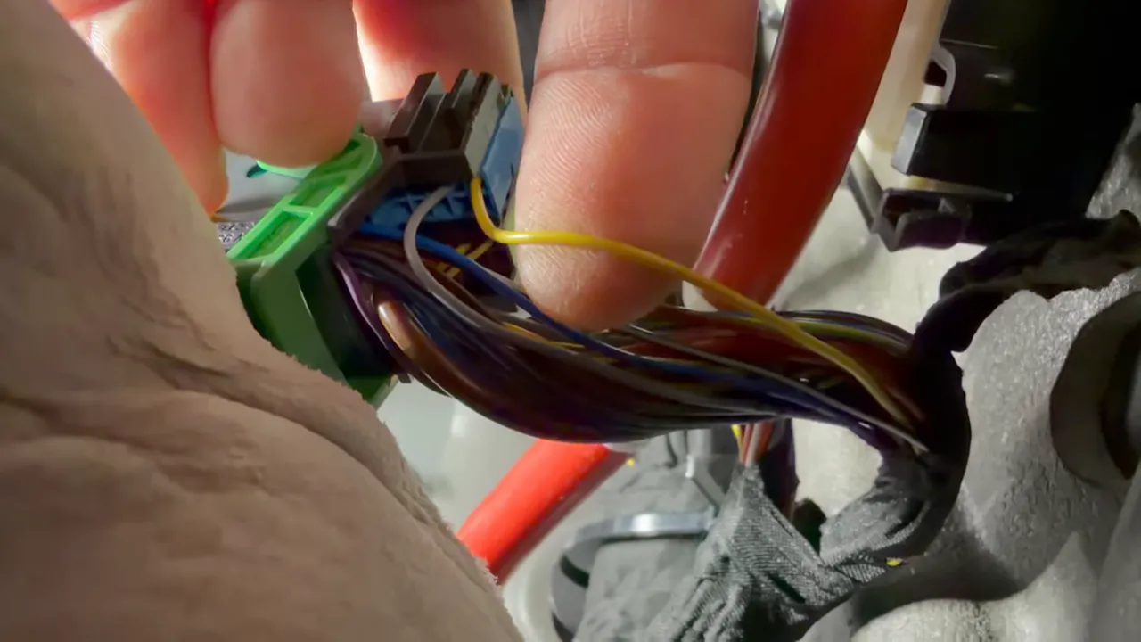 BMW passenger kick panel connector with yellow ignition sense wire exposed and hand for scale