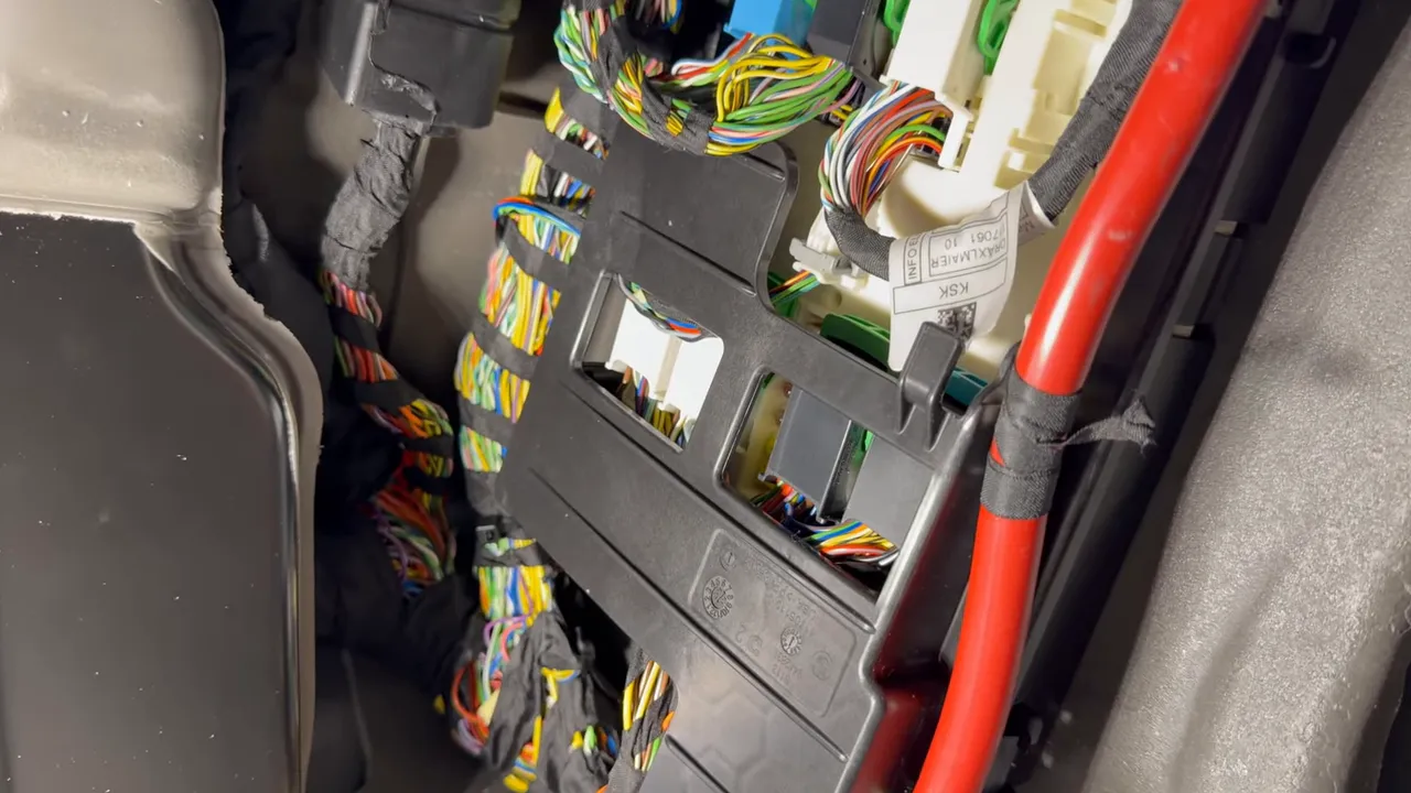 close-up of passenger kick panel connector showing multicolour wiring, connector slots and a red power cable