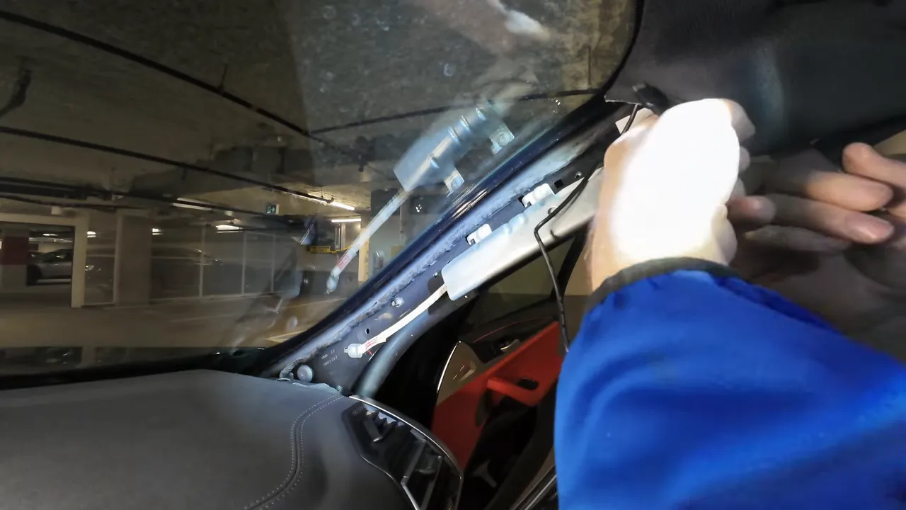 installer's hands tucking rear camera cable behind the A‑pillar near the airbag