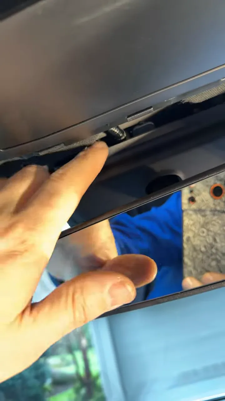 Finger pointing at a small cable tucked into the gap behind the center trim near the rear view mirror