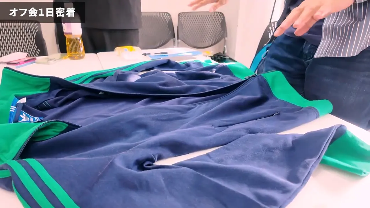テーブルに広げた紺と緑のトラックジャケットを両手で整える参加者