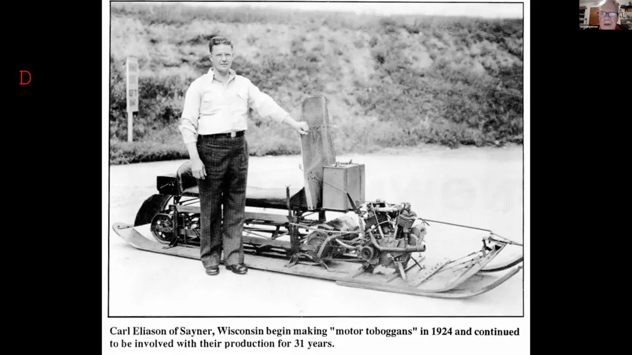 Carl Eliason standing next to an early motor toboggan (motorized sled) showing engine and chassis detail