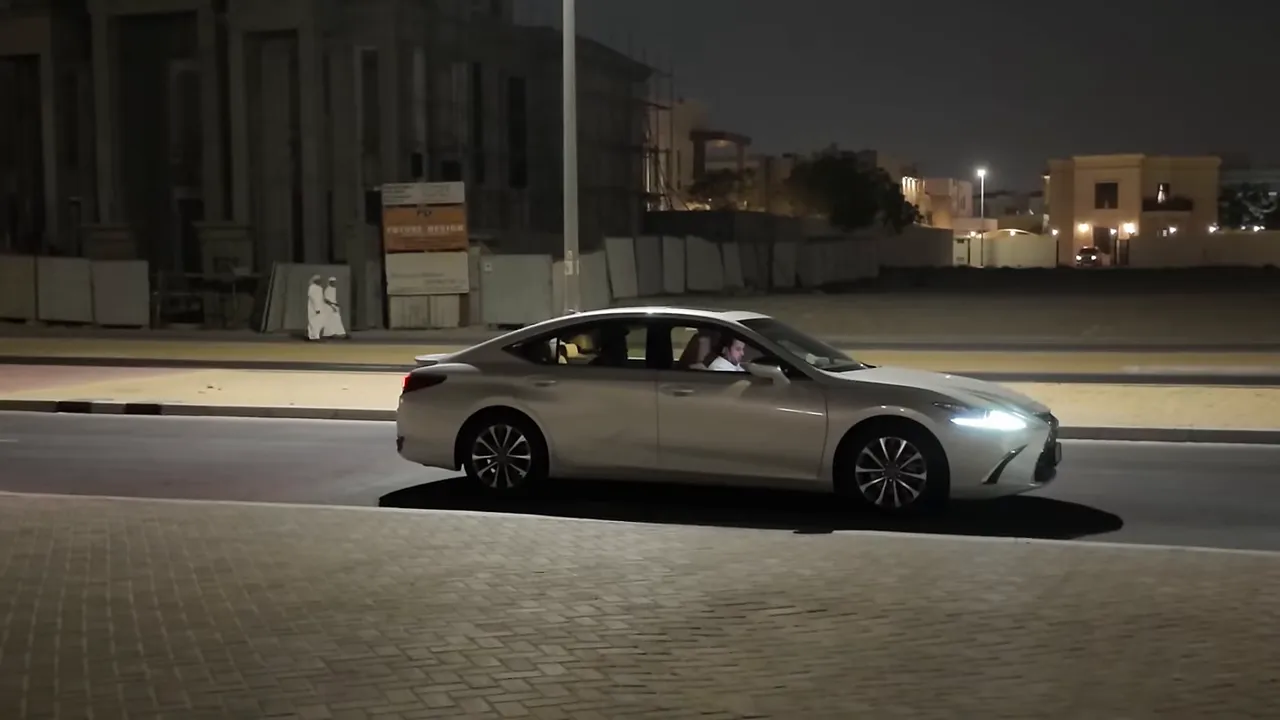 Voiture grise sur une route la nuit à Dubaï, éclairage urbain et trottoir au premier plan