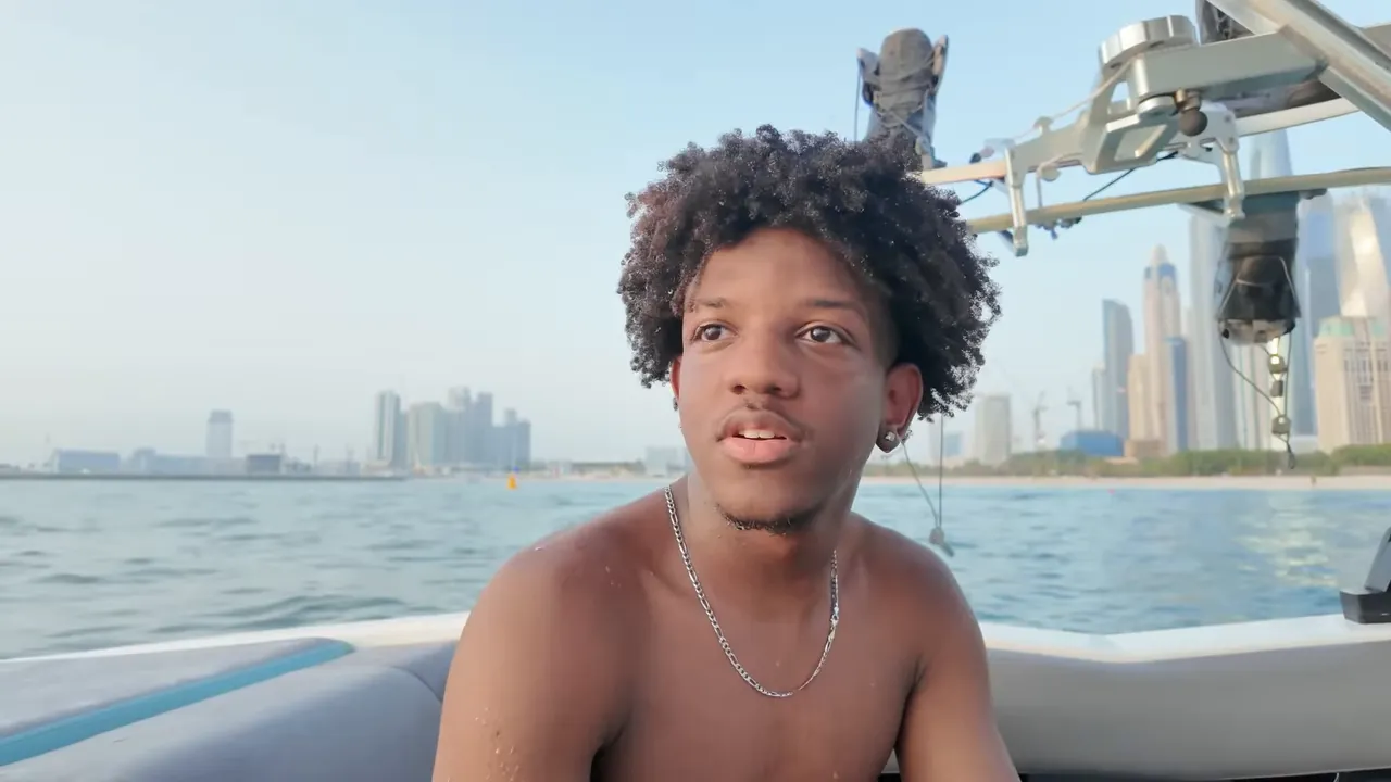 Jeune homme torse nu sur un bateau avec la skyline de Dubaï en arrière‑plan.