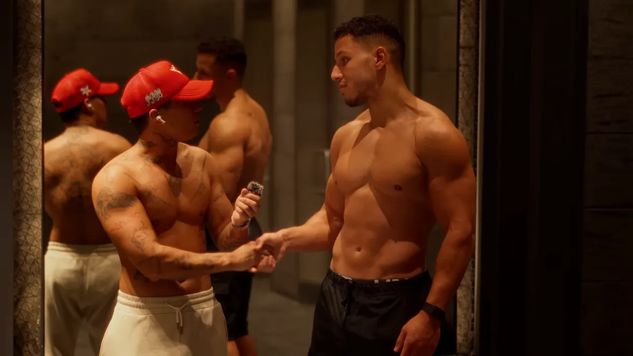 Deux hommes torse nu se serrent la main devant un miroir dans une salle de sport