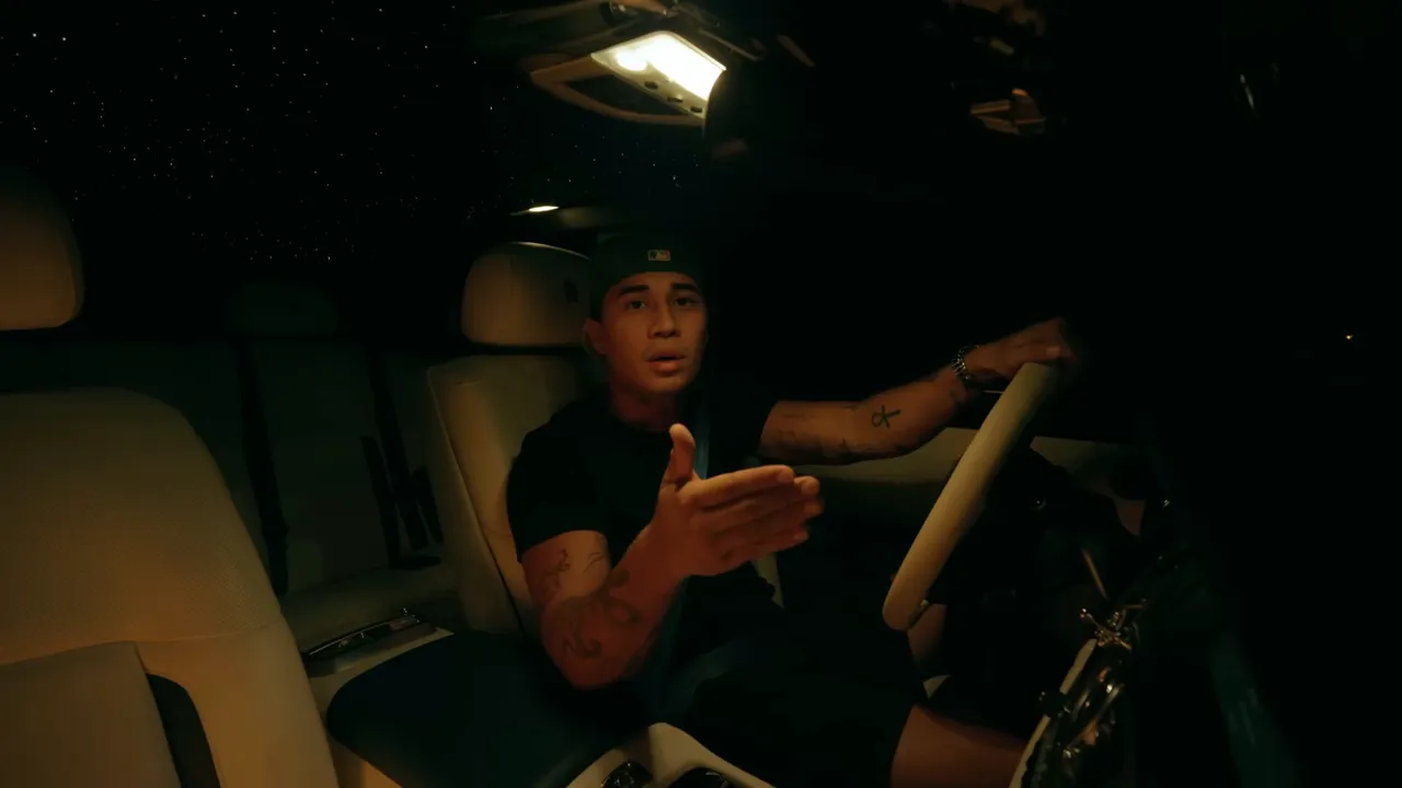 Auteur en voiture la nuit, geste de la main vers la caméra