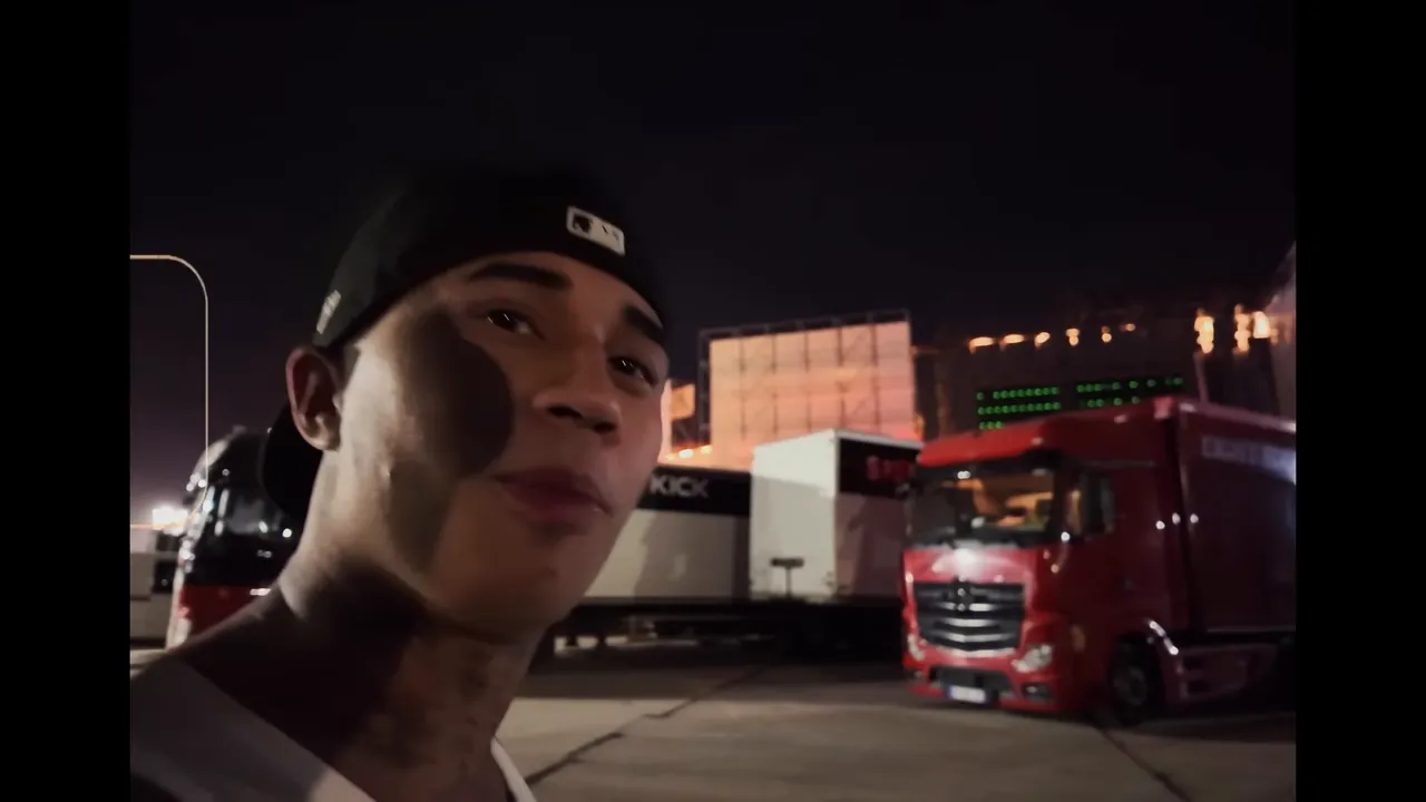 Personne en backstage devant des camions et la scène éclairée la nuit, ambiance festival